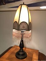 Full view of lamp on table showing black base and illuminated beaded shade