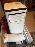 Front view of air conditioner with hose, window kit, remote