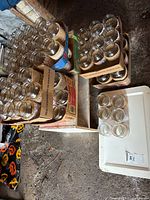 Multiple cartons holding rows of clear glass mason jars of two sizes with decorative wraps