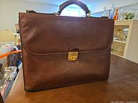 Front view showing leather surface, push-lock closure, top handle