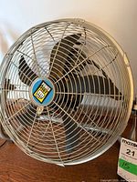 Front view of Power Fist floor fan showing metal grill, brand badge, black blades