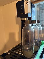 Sparkling water maker with three bottles on drip tray