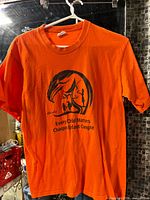 Front view of orange graphic T-shirt on hanger