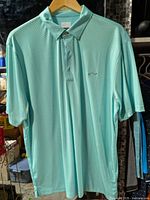 Full front view of Greg Norman turquoise geometric polo shirt on hanger
