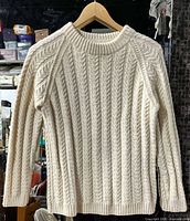 Front view of cream cable knit sweater on hanger