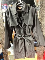 Full view of black trench coat hanging, shows overall style and condition