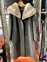 Front view of full-length black wool coat with beige fur collar on hanger
