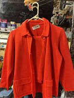 Front view of red wool blazer and matching skirt on hanger, brand tag visible