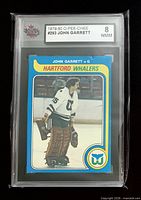 Front view of encapsulated 1979-80 O-Pee-Chee John Garrett #293 card showing player image and KSA grade label 8 NMM