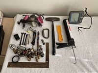 Overall contents laid out on towel: fish finder, caulking gun, hammer, respirator, wrenches, drill bits, knife, scraper, square, brass fittings