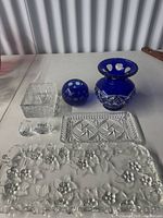 All seven crystal pieces laid out: cobalt flared vase, cobalt round bowl, square dish, rectangular tray, floral platter, two small salt cellars