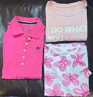 Three shirts laid flat: pink polo, pink text tee, white floral tee