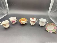 Front view of five teacups and one saucer, showing variety of patterns and shapes