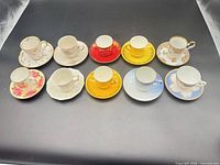 All eight demitasse cup-and-saucer pairs grouped on dark background