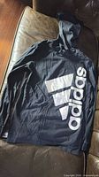 Full view of black Adidas thin hoodie laid flat showing front with large white logo