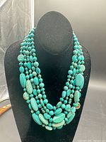 Full view of five-strand turquoise-coloured bead necklace on display bust
