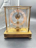 Full view of clock within glass case on wood base