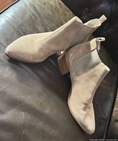 Side view of both taupe suede ankle boots on leather surface