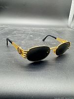 Angled side view of entire sunglasses showing gold frame and black lenses