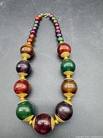 Full view of necklace laid flat showing large multicoloured beads and gold-toned spacers