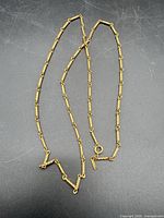Full view of gold plated bar-link necklace arranged on dark background