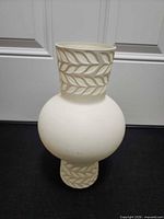 Front view of white matte ceramic vase showing full shape and carved leaf band on neck and base