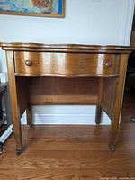 Front view of oak writing desk showing drawer, legs, and wooden casters
