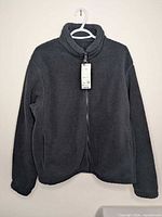 Front view of dark gray fleece jacket on hanger with tags visible