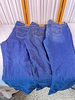 Three pairs of Levi's blue jeans laid flat showing back pockets and leather patches