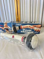 Massager in plastic wrap beside branded box