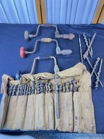 Full lot showing three brace drills, auger bits inside canvas roll and four long loose bits