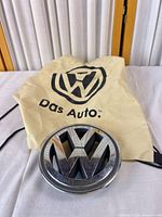 Front view of chrome and black Volkswagen wheel center cap emblem with drawstring bag