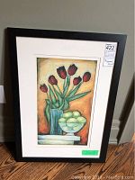 Framed print leaning against wall showing full artwork with tulips and bowl of green apples