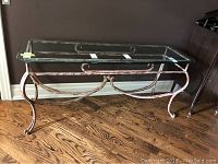 Full front view of the glass console table showing the clear rectangular glass top and curved distressed white metal frame.