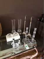 Image showing multiple pairs of candleholders on glass table including Tiffany crystal tall candleholders, pewter leaf design candleholders, and silverplate tall candleholders.