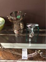 Photo showing the nautical style hurricane lantern with metal accents and the modernist glass vase with metal insert on a glass surface.
