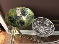Two crystal bowls placed on glass table; one large green and black patterned colored crystal bowl, one smaller clear cut crystal bowl.