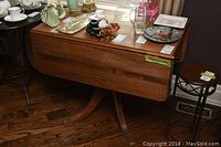 Photo showing full side view of the drop leaf table with one leaf down, displaying wood grain and some visible wear on surface.