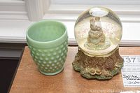 Green jadeite hobnail vase and Natures Friend musical snow globe with bunny inside glass dome on tree stump base.