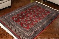 Full view of red Bukhara rug with fringe on hardwood floor