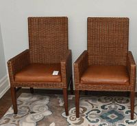 Two wicker chairs with brown leather seat cushions standing side by side on a patterned rug