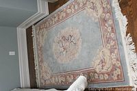 Full view of rectangular wool area rug with central peacock motif and floral borders, laid on hardwood floor.