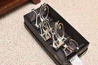 Four silver metal Christmas stocking hooks arranged in a box, spelling JOY, three matching designs, one different.