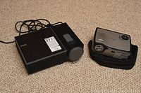 Two projectors shown side-by-side, Dell projector with black casing and Optoma with silver casing on carrying pouch.