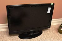 Front view of the 31-inch Samsung TV showing the black bezel and stand with sticker on top-right corner.
