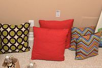 Five decorative pillows arranged against a wall showing their various patterns and sizes: solid red, circular pattern, and multicolor chevron pattern.
