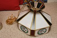 Full view of the leaded glass Tiffany style swag lighting fixture showing white, black, and burgundy stained glass panels with brass-colored chain and mount on a carpet.