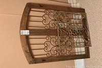 Photo of wood framed faux window grate leaning against a wall with a smaller metal decorative grate placed on top.