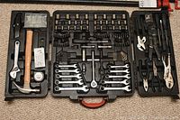 Full view of open black molded plastic carrying case with hammer, wrenches, sockets, screwdriver bits and pliers neatly arranged inside.