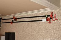 Three large industrial metal clamps arranged on carpeted floor showing full length and red clamp mechanism.